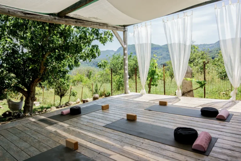 Open-sided yoga shala with white curtains, mats and a view of the hills