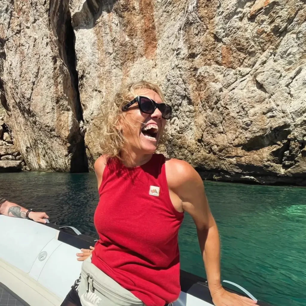 A guest laughing on the boat in front of a rock face and turquoise water