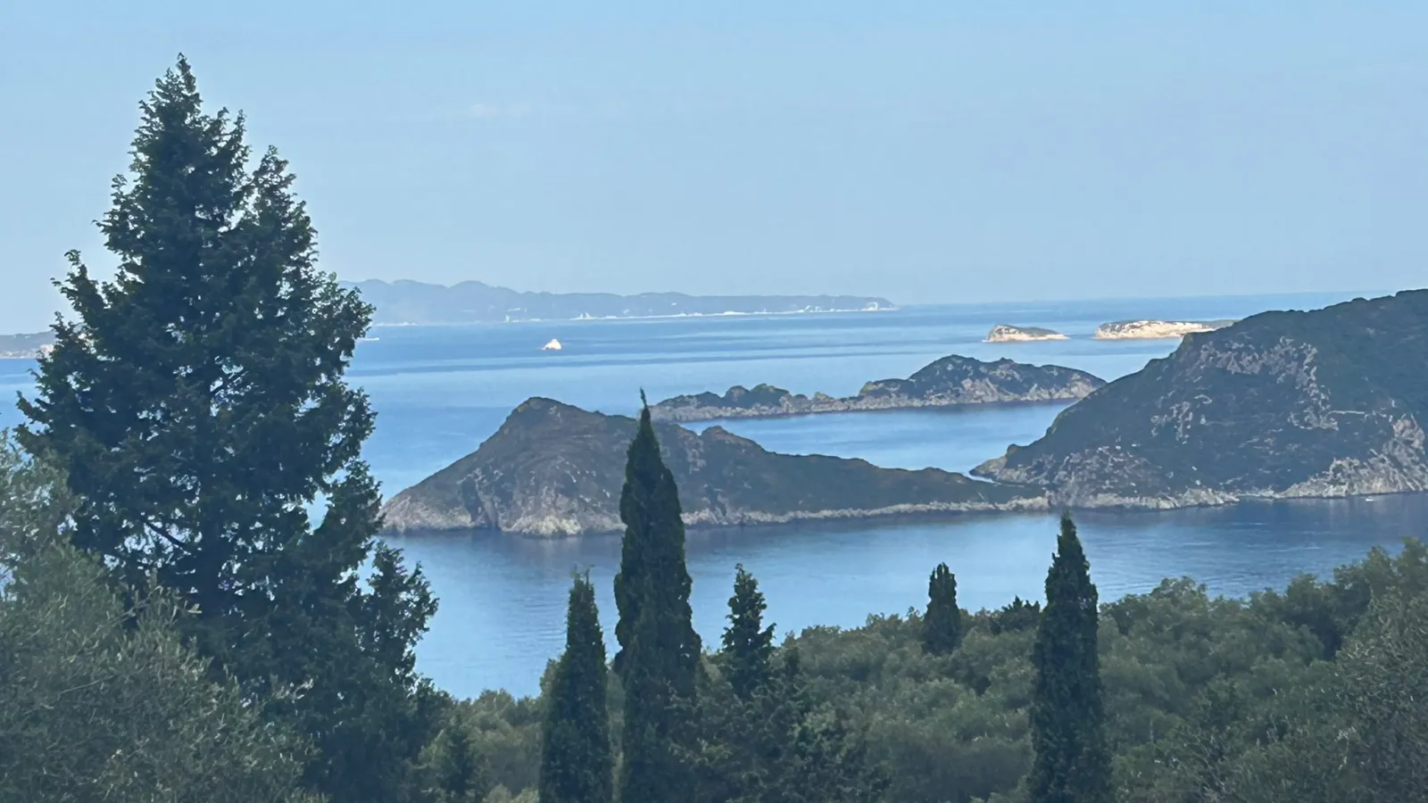 View across the Ionian Sea to the headlands of northwest Corfu, framed by cypress trees